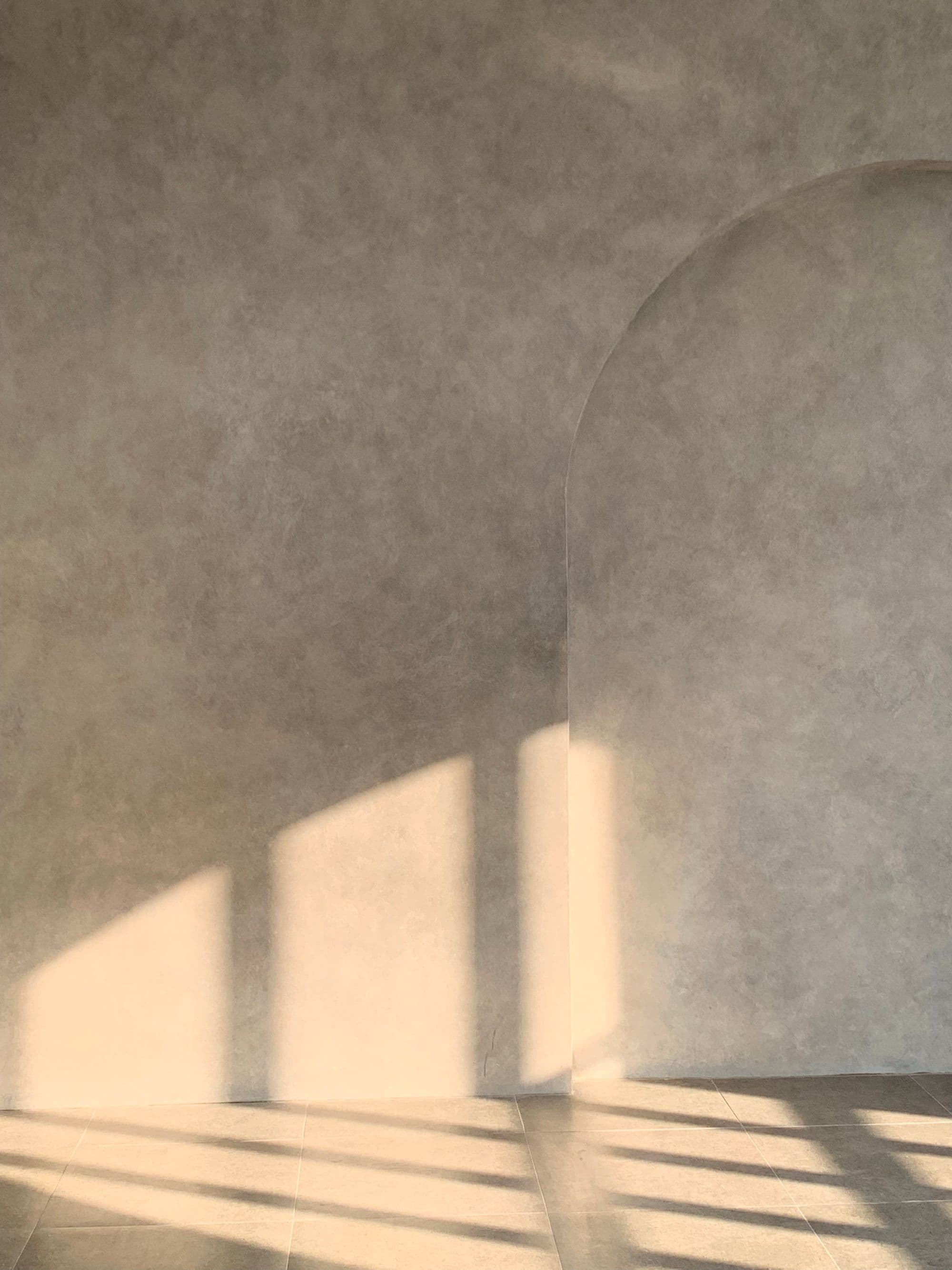Soft plaster wall with an arched niche and long window shadows