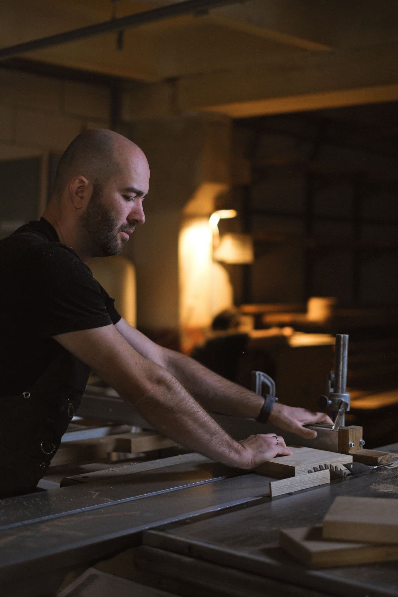 Joiner feeding a length of oak through a table saw in a warmly lit workshop